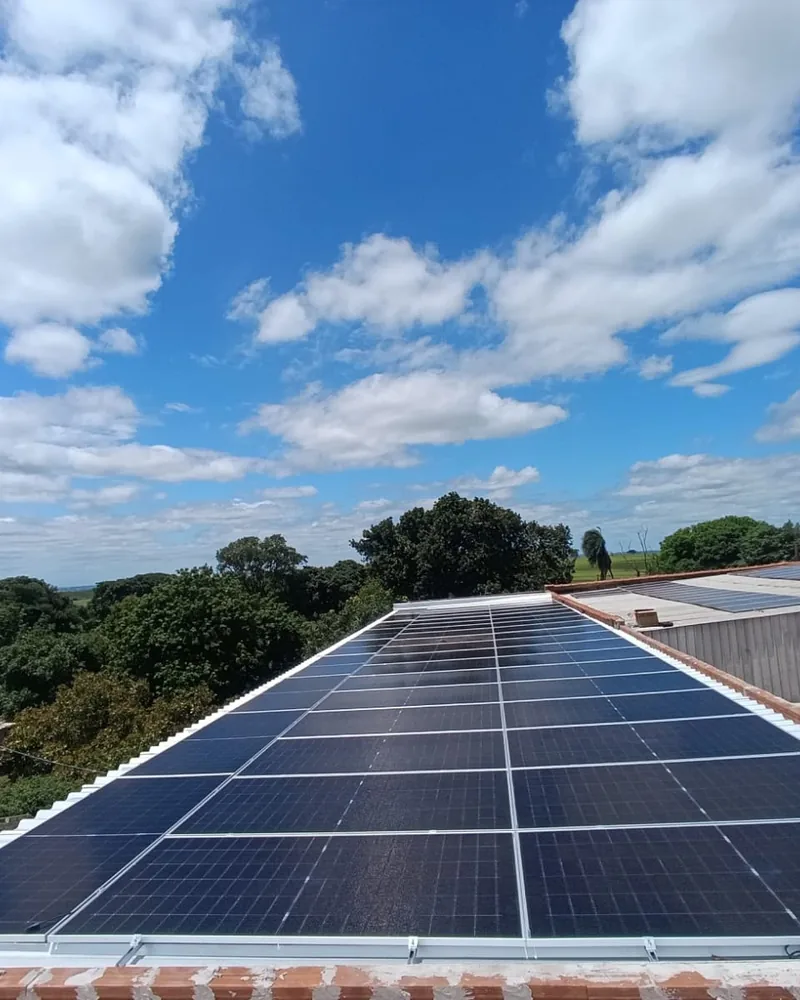 Painéis solares instalados em telhado de laje, com céu azul e nuvens ao fundo