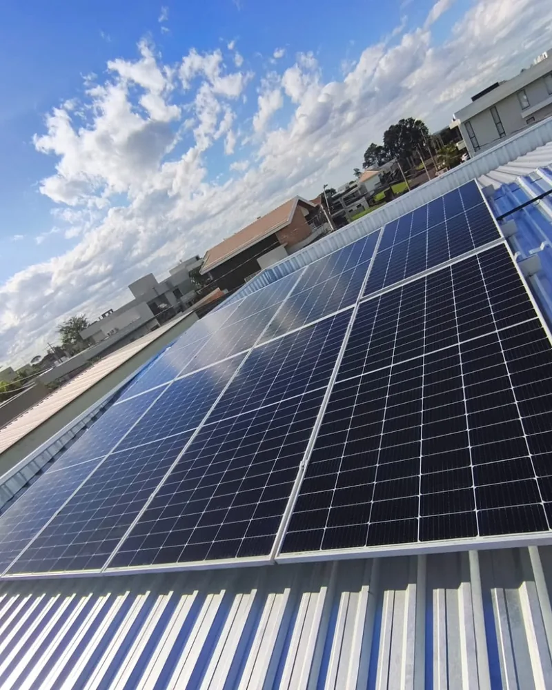 Painéis fotovoltaicos em telhado metálico sob céu com nuvens