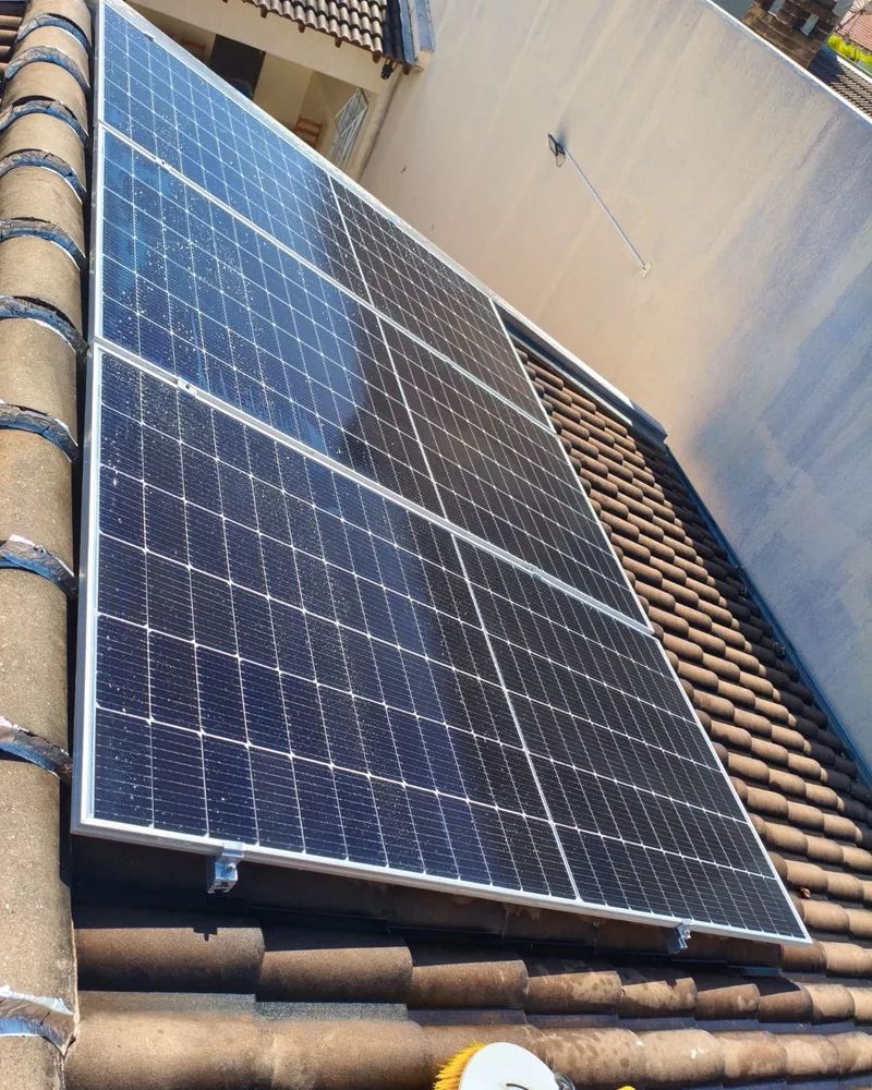 Detalhe de painéis fotovoltaicos fixados em telhado de telhas coloniais